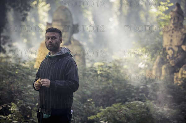 Caucasian man exploring ancient statues in forest