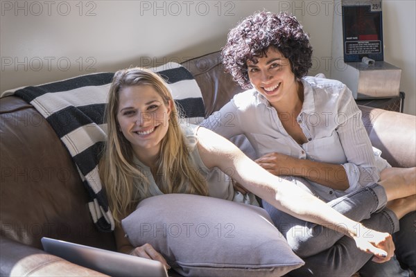 Caucasian lesbian couple smiling on sofa