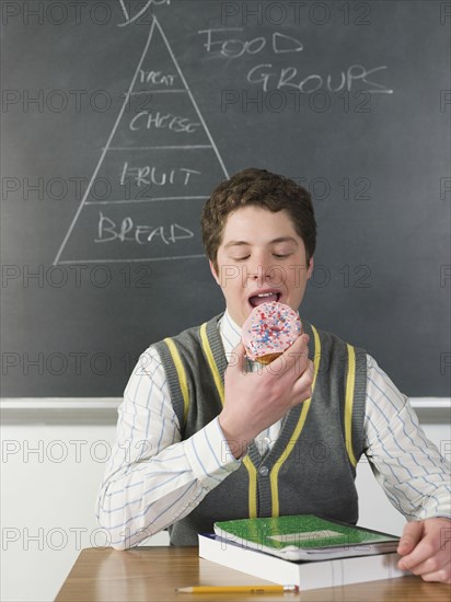 Student eating donut at chalkboard in classroom