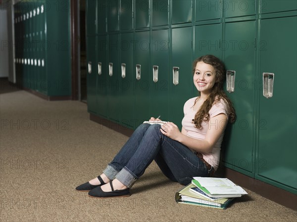 Mixed race student sitting at locker in school hallway