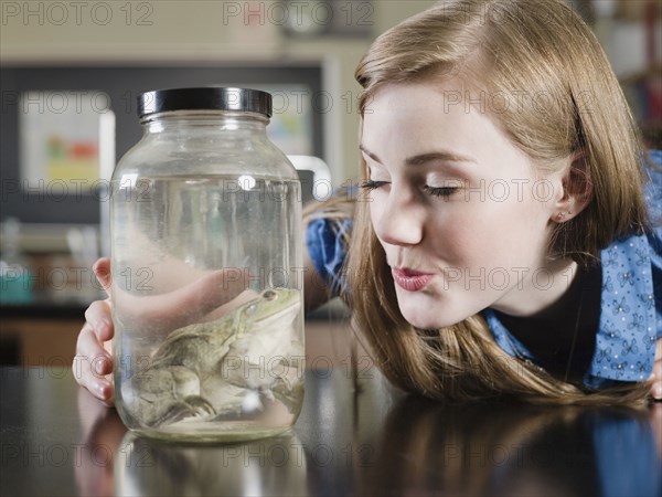 Student examining frog in jar in classroom