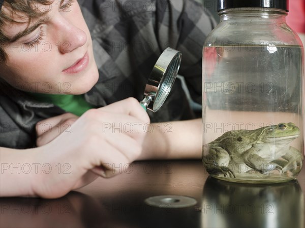 Student examining frog in jar in classroom