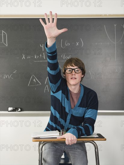 Student raising his hand at desk in classroom