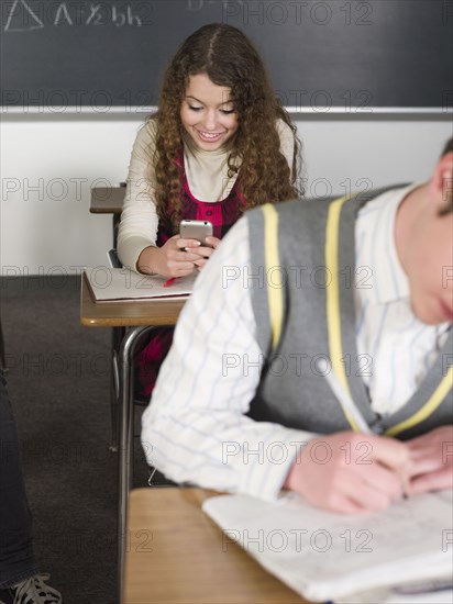 Student using cell phone at desk in classroom