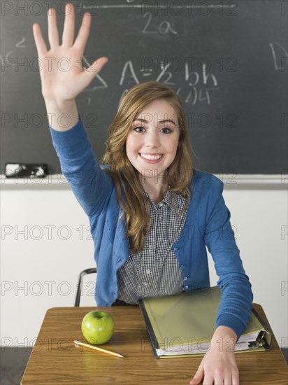 Student raising hand at desk in classroom