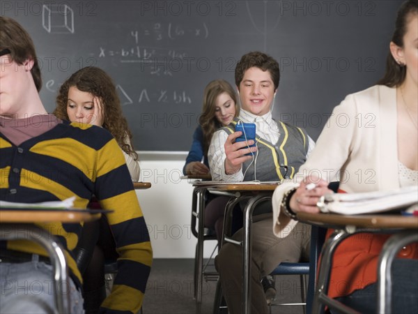 Student listening to earbuds at desk in classroom