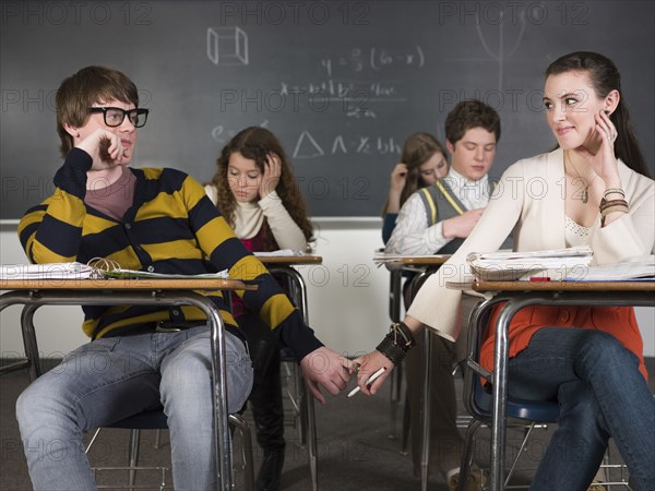 Students holding hands at desks in classroom