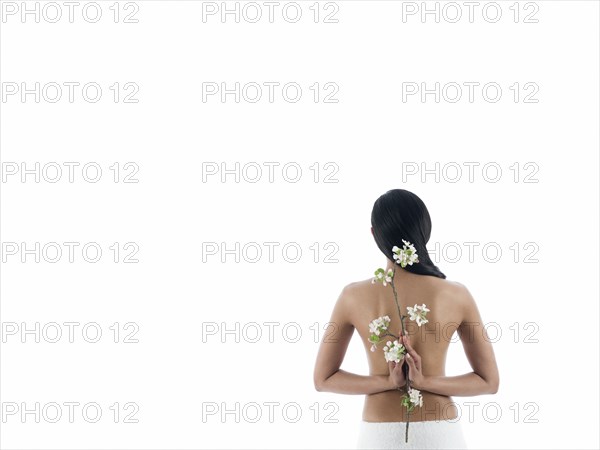 Rear view of nude woman holding flowers behind back