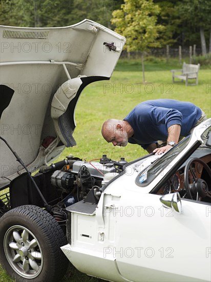 Older man examining broken-down convertible in park
