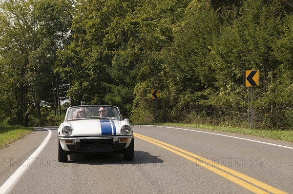 Older couple driving convertible on rural road