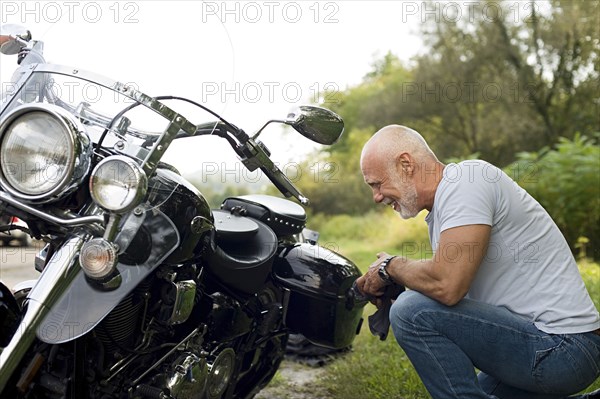Older man repairing motorcycle in park