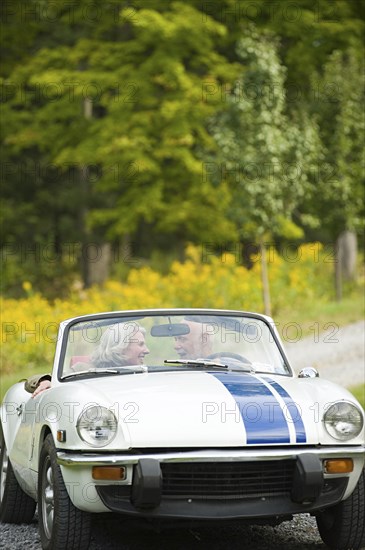 Older couple driving convertible on dirt road