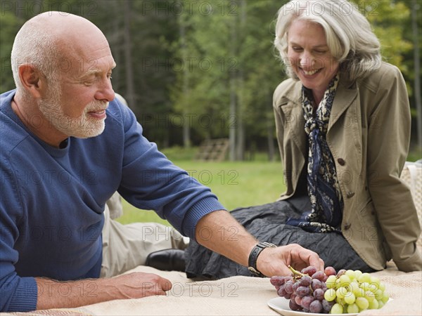 Older couple eating grapes at picnic in park