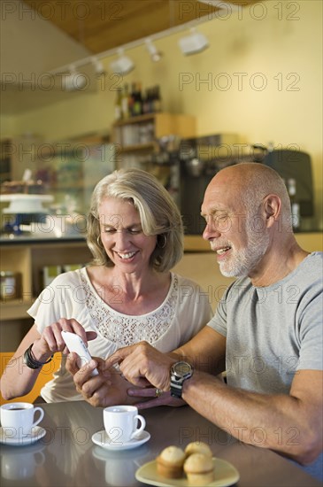 Older couple using cell phone in cafe