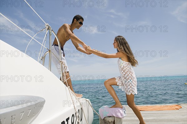 Man helping girlfriend into sailboat on harbor