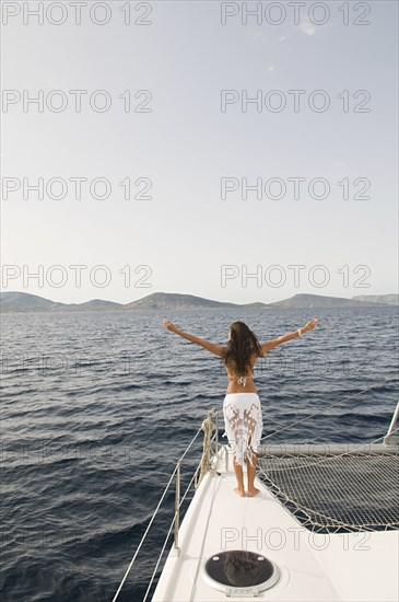 Woman standing with arms outstretched on sailboat deck