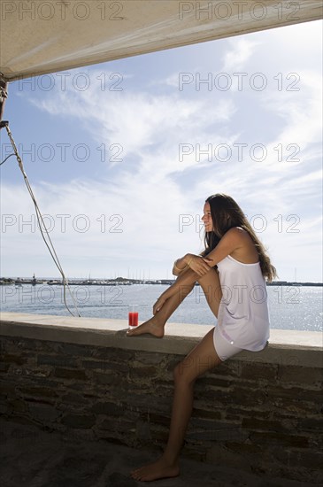 Woman sitting on wall overlooking ocean
