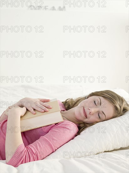 Caucasian woman napping with book on bed