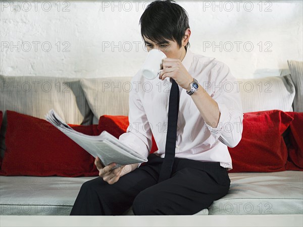 Asian businessman reading newspaper on sofa