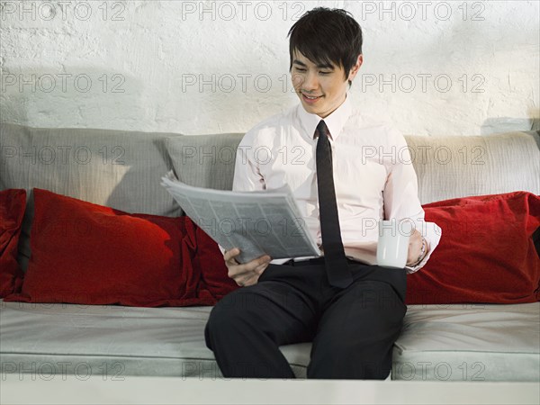 Asian businessman reading newspaper on sofa