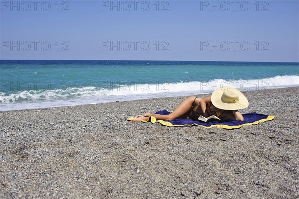 Woman sunbathing and reading on beach
