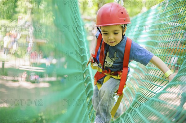 Caucasian boy in harness climbing on net