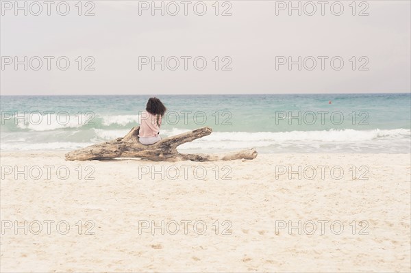 Woman sunbathing on driftwood log on beach