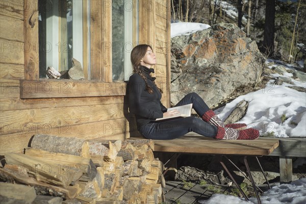Caucasian woman reading book on cabin porch
