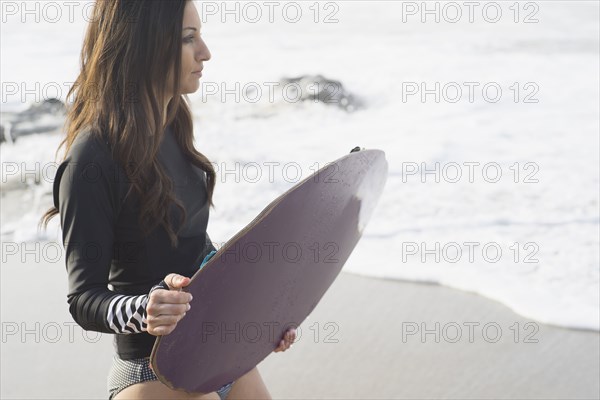 Caucasian woman holding skimboard at beach