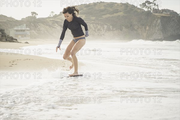 Caucasian woman riding skimboard at beach