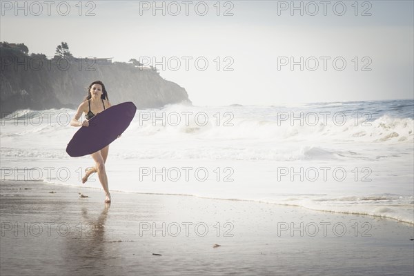 Caucasian woman running with skimboard at beach