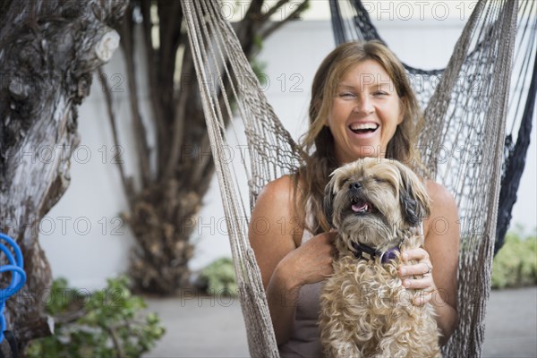 Caucasian woman in hammock holding dog and laughing