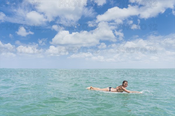 Caucasian woman paddling on surfboard in ocean