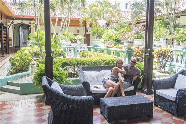 Smiling Caucasian couple on sofa in hotel courtyard