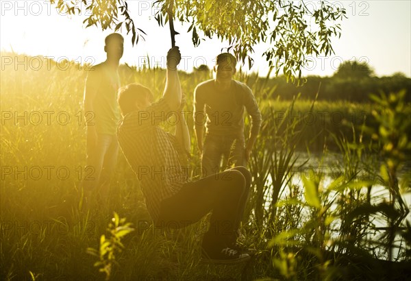 Caucasian men playing on rope swing at lake