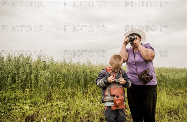 Caucasian mother and son taking photographs in rural field