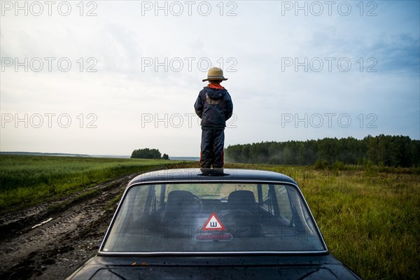 Caucasian boy standing on car roof in rural field