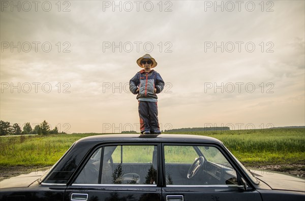 Caucasian boy standing on car roof in rural field