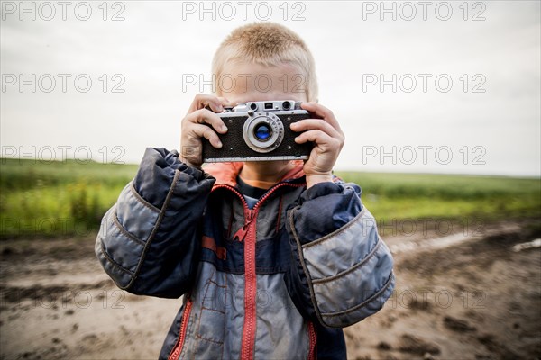 Caucasian boy taking photograph in rural field