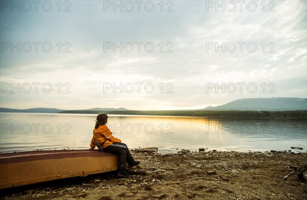 Caucasian woman sitting on dilapidated boat at rural lake