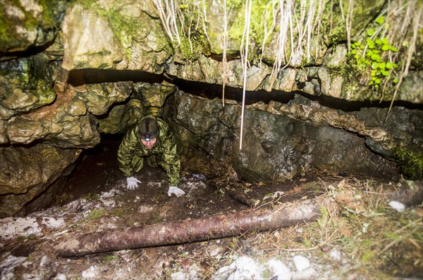 Caucasian man climbing out of rock formation cave