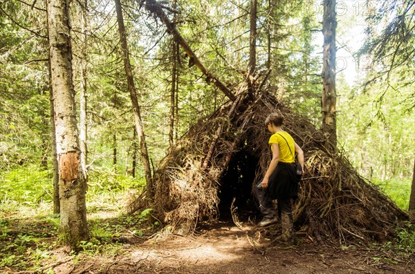 Caucasian boy playing in thatched teepee fort in forest