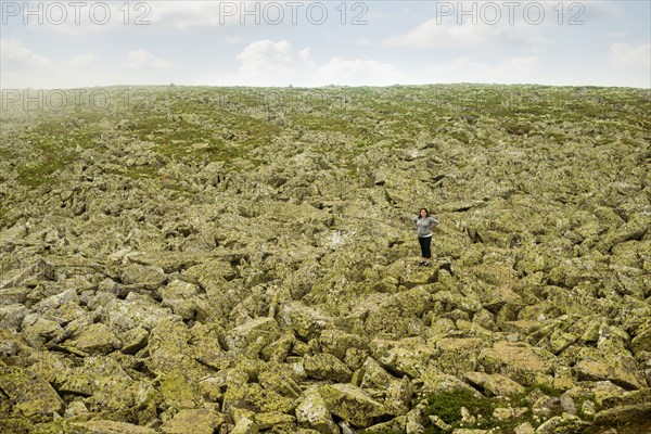 Caucasian hiker standing with arms outstretched in rocky field