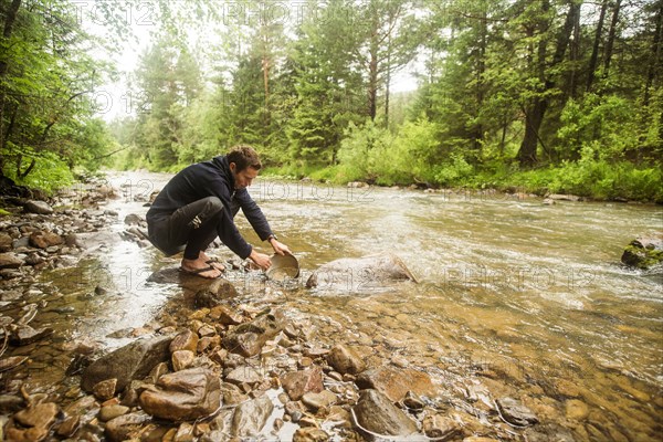 Caucasian man crouching in forest river