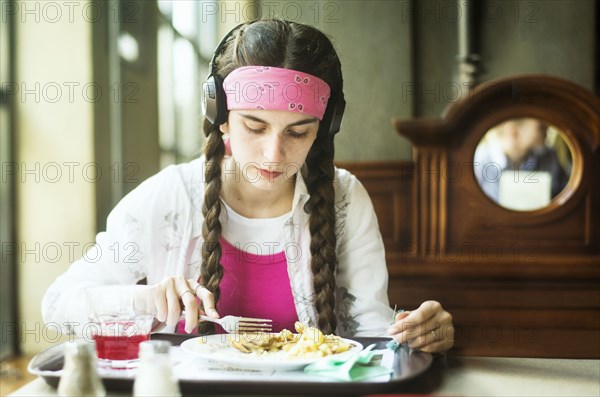 Caucasian woman wearing headphones eating in dining room