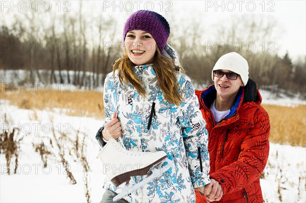 Caucasian couple carrying ice skates in snowy field