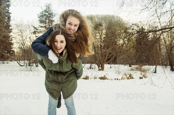 Caucasian woman carrying friend piggyback in snowy field