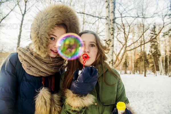Caucasian women blowing bubbles in snowy field