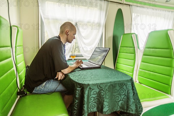 Caucasian man using laptop in green booth on train