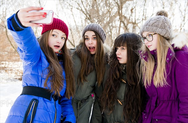 Caucasian girls taking cell phone photograph in snowy field